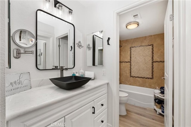 full bathroom featuring tiled shower / bath, hardwood / wood-style floors, vanity, and toilet