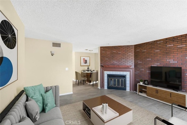 living room with a tiled fireplace, light hardwood / wood-style flooring, and a textured ceiling