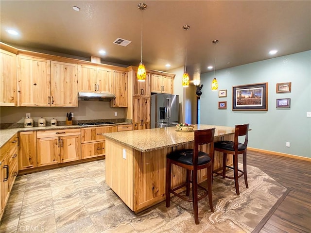 kitchen with a kitchen bar, high end fridge, a kitchen island, pendant lighting, and light stone countertops