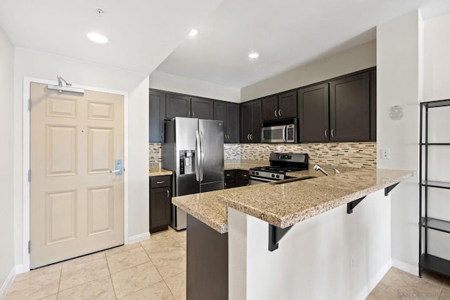 kitchen with a kitchen breakfast bar, kitchen peninsula, stainless steel appliances, light stone countertops, and backsplash