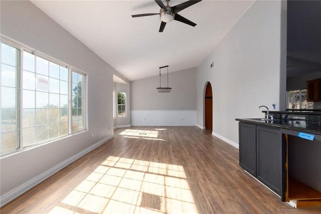 unfurnished living room with hardwood / wood-style flooring, vaulted ceiling, sink, and ceiling fan