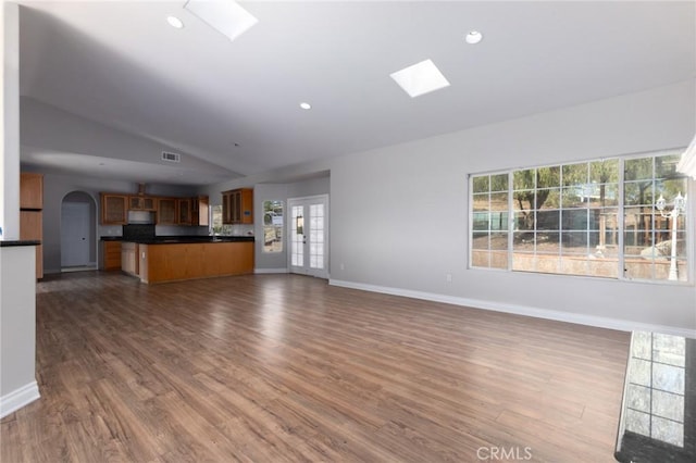 unfurnished living room featuring dark wood-type flooring, french doors, and vaulted ceiling with skylight