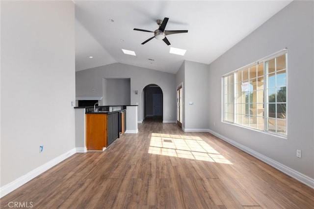 unfurnished living room featuring dark hardwood / wood-style flooring, sink, vaulted ceiling with skylight, and ceiling fan