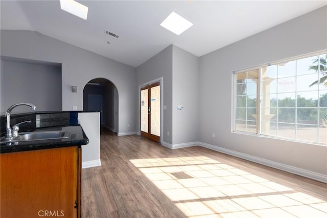 kitchen featuring vaulted ceiling with skylight, light hardwood / wood-style floors, and sink