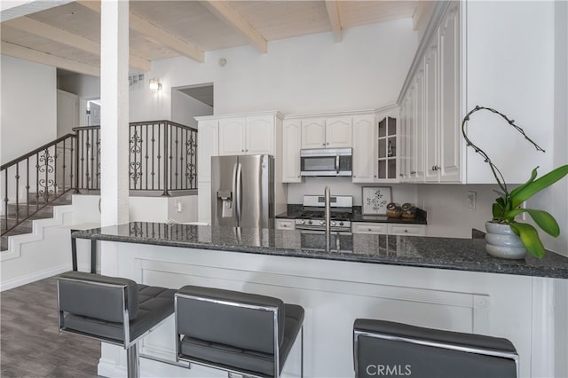 kitchen with dark stone countertops, beamed ceiling, appliances with stainless steel finishes, and white cabinets