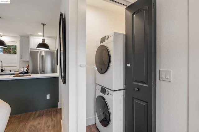 clothes washing area featuring stacked washing maching and dryer, sink, and dark hardwood / wood-style flooring