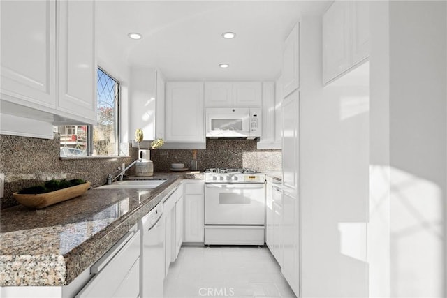 kitchen featuring sink, white cabinets, dark stone counters, decorative backsplash, and white appliances