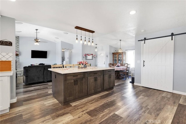 kitchen featuring lofted ceiling, dark brown cabinetry, an island with sink, pendant lighting, and a barn door