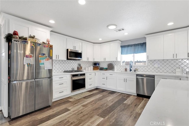 kitchen featuring sink, appliances with stainless steel finishes, white cabinetry, backsplash, and dark hardwood / wood-style flooring