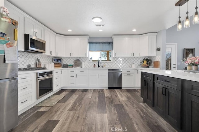 kitchen with hanging light fixtures, white cabinetry, appliances with stainless steel finishes, and dark hardwood / wood-style flooring