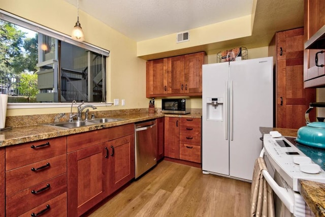 kitchen with sink, appliances with stainless steel finishes, hanging light fixtures, light hardwood / wood-style floors, and light stone countertops