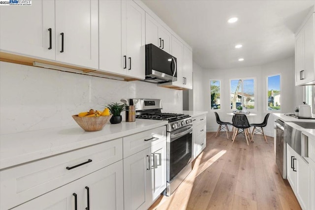 kitchen with white cabinetry, tasteful backsplash, light hardwood / wood-style flooring, stainless steel appliances, and light stone countertops