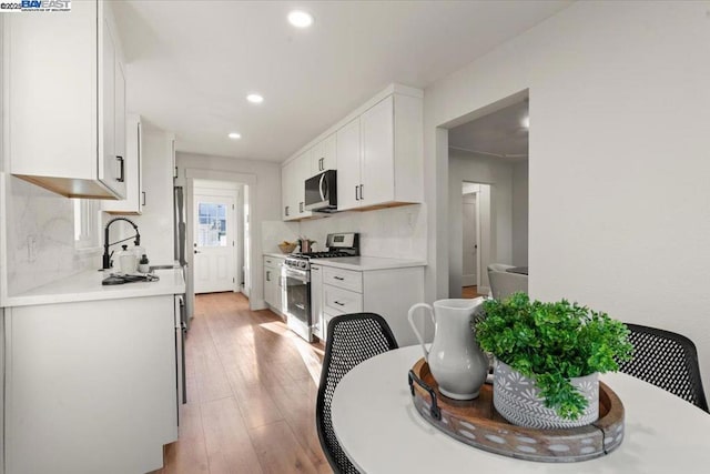 kitchen featuring sink, white cabinetry, light wood-type flooring, appliances with stainless steel finishes, and backsplash