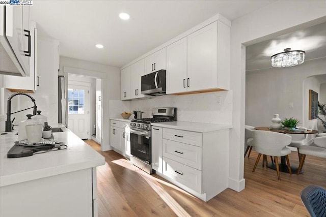 kitchen featuring decorative backsplash, appliances with stainless steel finishes, white cabinets, and light hardwood / wood-style flooring