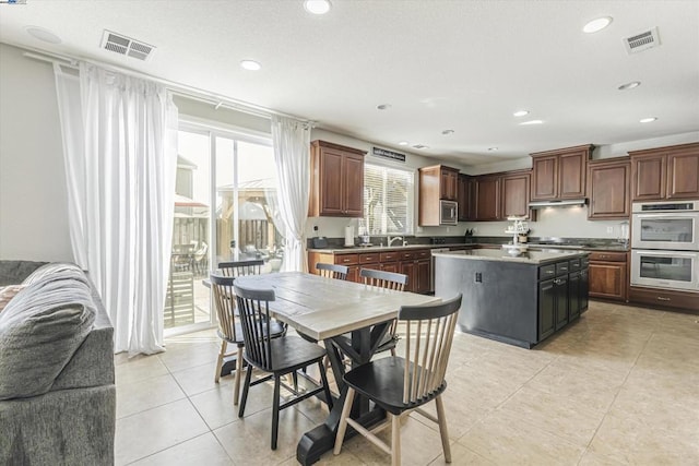 kitchen with appliances with stainless steel finishes, sink, a center island, light tile patterned floors, and dark brown cabinetry