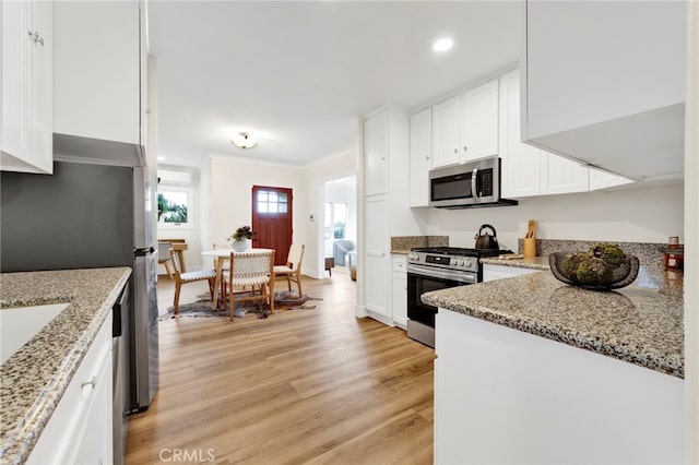 kitchen with appliances with stainless steel finishes, white cabinetry, light stone counters, ornamental molding, and light wood-type flooring