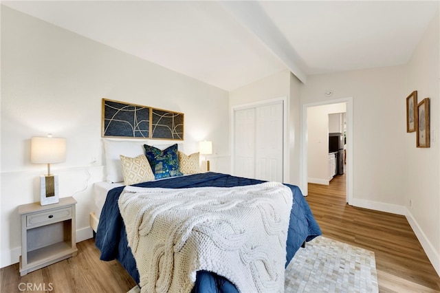 bedroom with hardwood / wood-style floors, a closet, and vaulted ceiling with beams