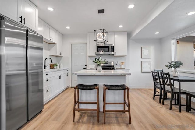 kitchen with white cabinetry, decorative light fixtures, a center island, stainless steel appliances, and light hardwood / wood-style floors