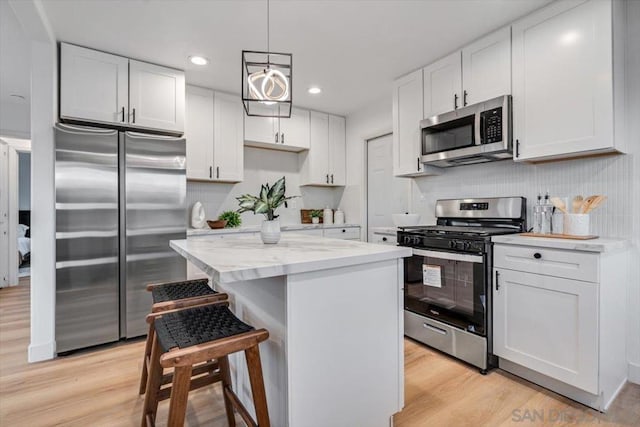 kitchen with white cabinetry, hanging light fixtures, stainless steel appliances, light hardwood / wood-style floors, and a kitchen island