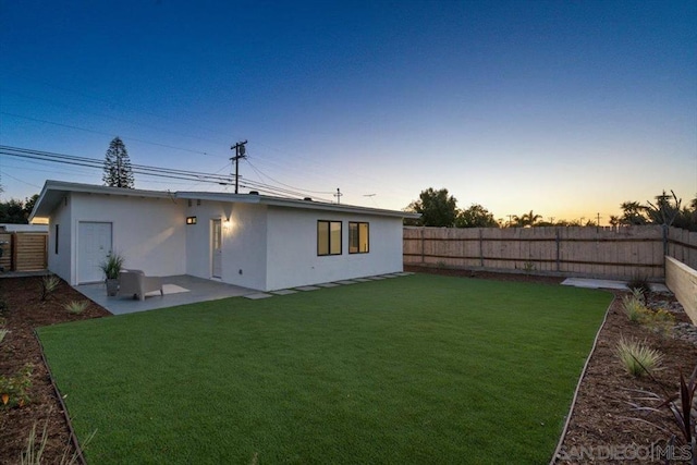 back house at dusk with a lawn and a patio area