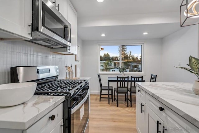 kitchen with pendant lighting, stainless steel appliances, light stone countertops, and white cabinets