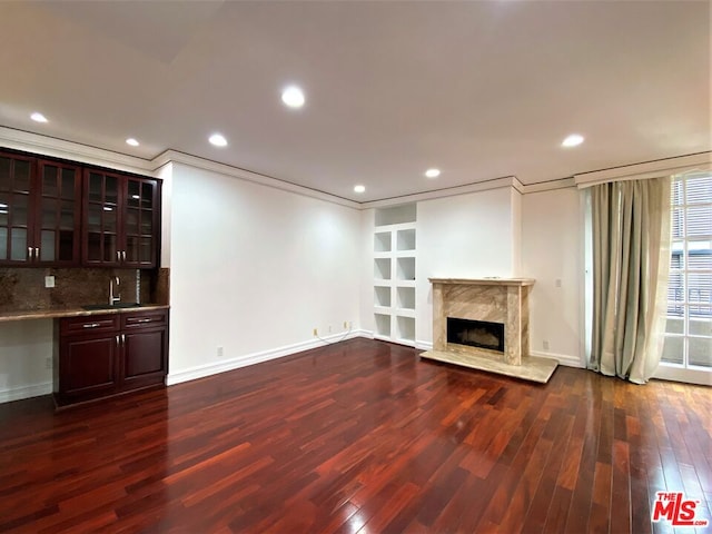 unfurnished living room with crown molding, dark wood-type flooring, sink, and a fireplace