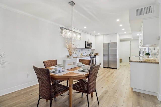 dining area with sink, ornamental molding, and light wood-type flooring