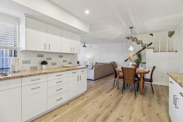 kitchen featuring white cabinetry, decorative backsplash, ceiling fan, light stone counters, and light hardwood / wood-style flooring