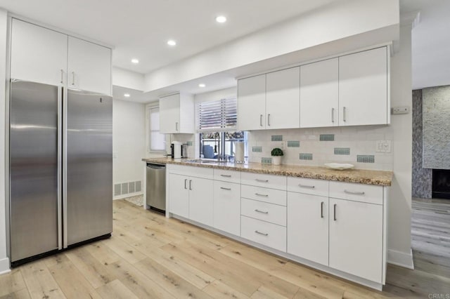 kitchen with white cabinetry, light hardwood / wood-style flooring, stainless steel appliances, light stone countertops, and backsplash