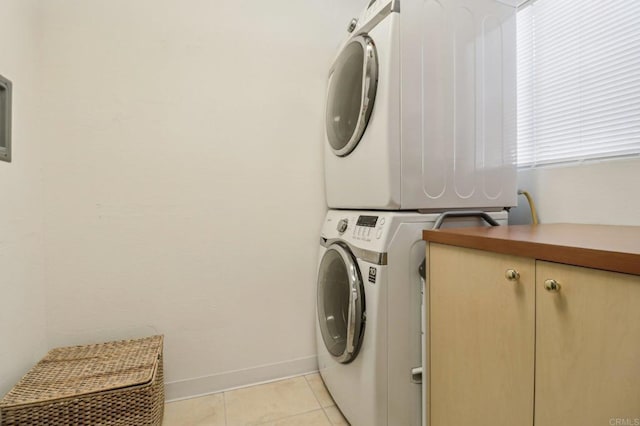 laundry area featuring stacked washer / dryer, light tile patterned flooring, and cabinets