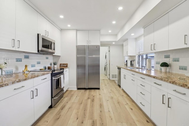 kitchen featuring sink, light hardwood / wood-style flooring, appliances with stainless steel finishes, white cabinetry, and light stone counters