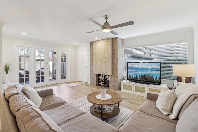 living room featuring ceiling fan, a large fireplace, light hardwood / wood-style floors, and french doors