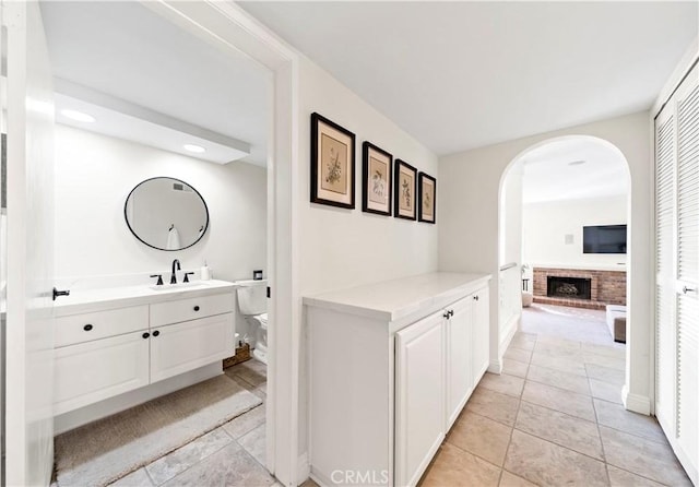 bathroom with vanity, a brick fireplace, tile patterned floors, and toilet