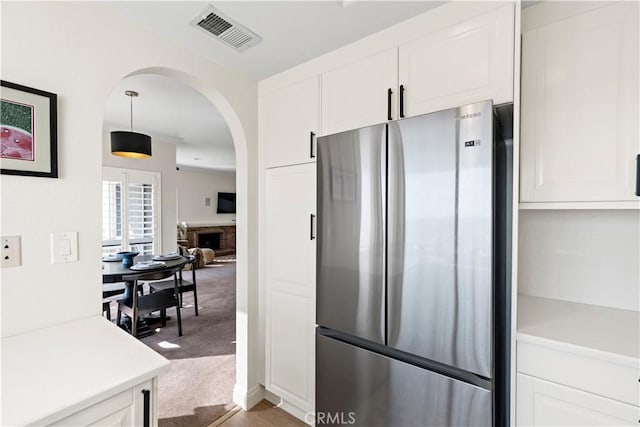 kitchen with hanging light fixtures, stainless steel refrigerator, white cabinets, and carpet flooring