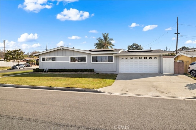 single story home featuring solar panels, concrete driveway, a front yard, fence, and a garage