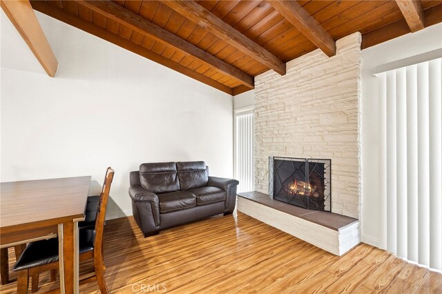 living room with lofted ceiling with beams, a stone fireplace, light hardwood / wood-style floors, and wooden ceiling