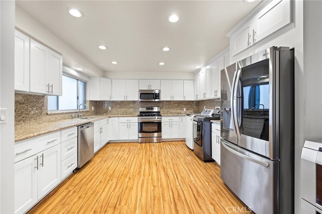 kitchen featuring appliances with stainless steel finishes, light stone countertops, light hardwood / wood-style floors, decorative backsplash, and white cabinets