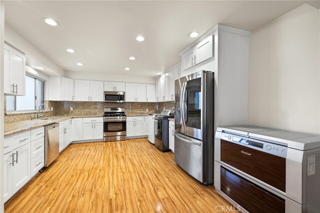 kitchen with sink, white cabinetry, stainless steel appliances, tasteful backsplash, and light wood-type flooring