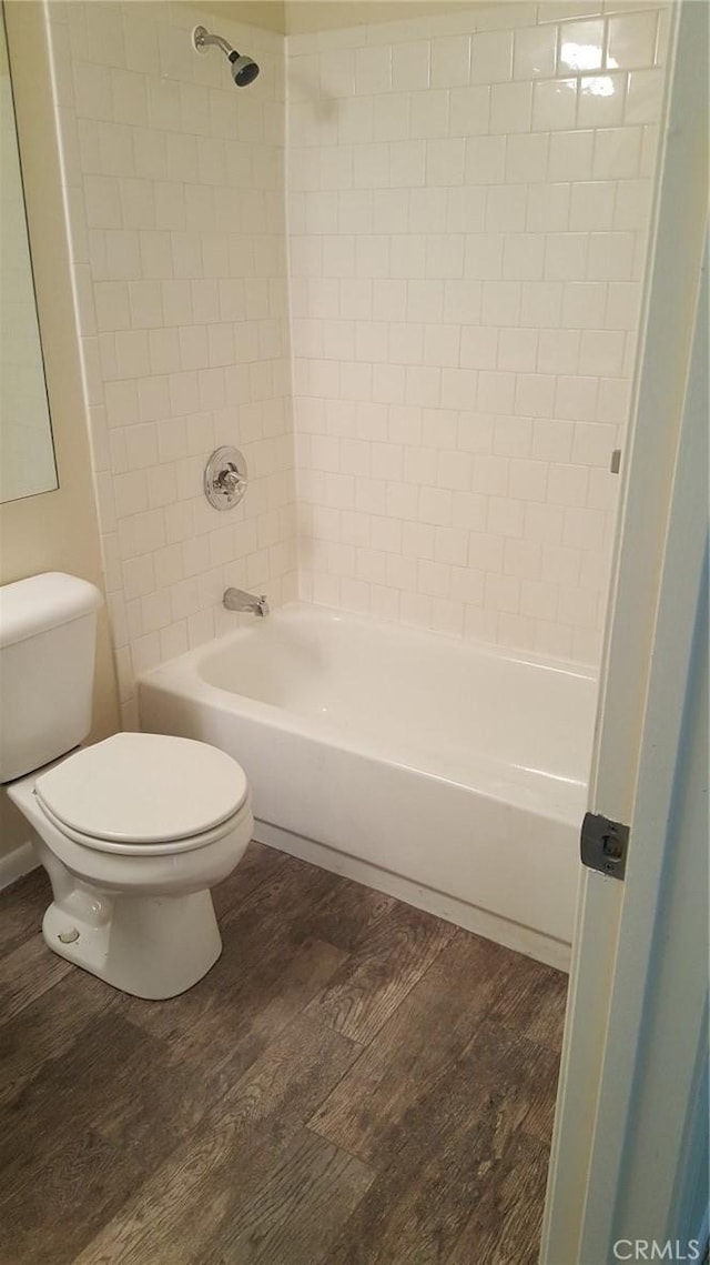 bathroom with hardwood / wood-style flooring, tiled shower / bath combo, and toilet