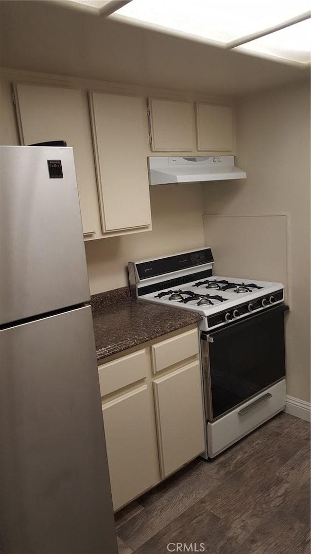 kitchen featuring dark stone countertops, white gas range, stainless steel fridge, and dark hardwood / wood-style floors