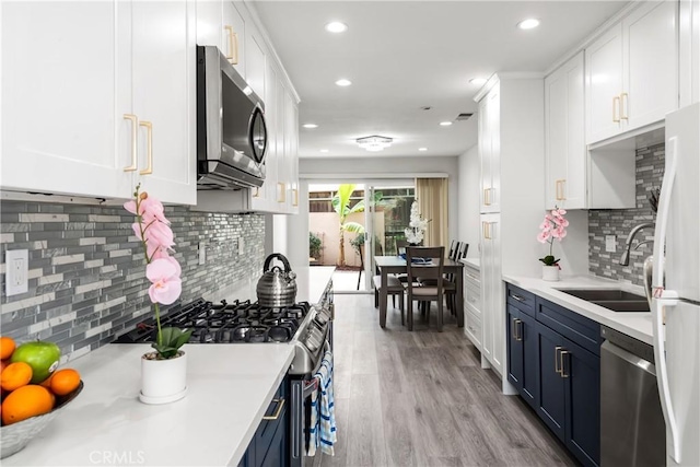 kitchen featuring blue cabinetry, sink, white cabinetry, light hardwood / wood-style flooring, and appliances with stainless steel finishes