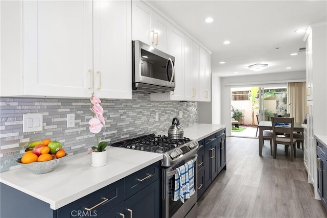 kitchen with blue cabinets, tasteful backsplash, light hardwood / wood-style flooring, stainless steel appliances, and white cabinets