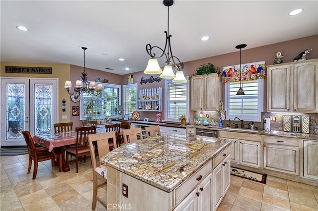 kitchen featuring a kitchen island, sink, light stone counters, and decorative light fixtures