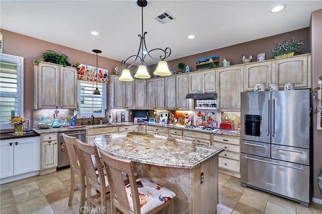 kitchen with appliances with stainless steel finishes, decorative light fixtures, sink, a center island, and light stone counters