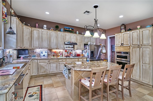 kitchen with light stone counters, appliances with stainless steel finishes, sink, and an island with sink