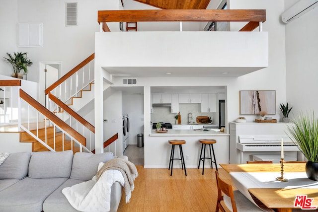 living room with an AC wall unit, sink, a high ceiling, independent washer and dryer, and light hardwood / wood-style floors