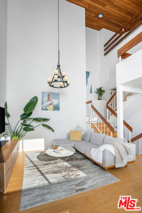 living room with a notable chandelier, wood ceiling, wood-type flooring, and a high ceiling