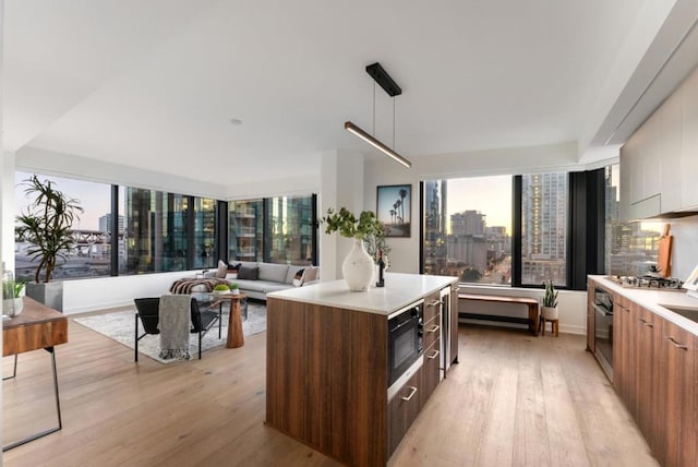 kitchen featuring stainless steel gas cooktop, a center island, light wood-type flooring, pendant lighting, and oven