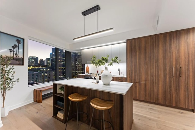 kitchen featuring decorative light fixtures, sink, a breakfast bar area, a kitchen island with sink, and light wood-type flooring