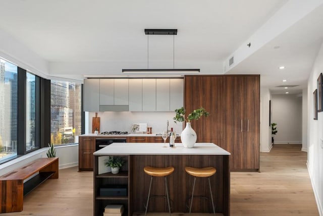 kitchen featuring a kitchen island with sink, hanging light fixtures, stainless steel gas stovetop, and light wood-type flooring